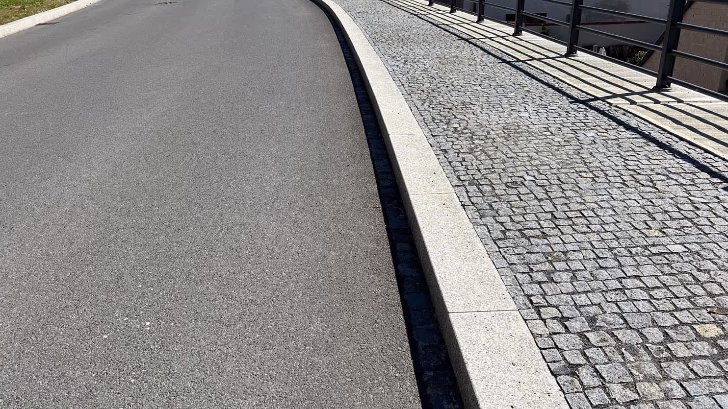 Chodník ze šedých žulových kostek, lemovaný řezaným obrubníkem, elegantně navazuje na asfaltovou vozovku.