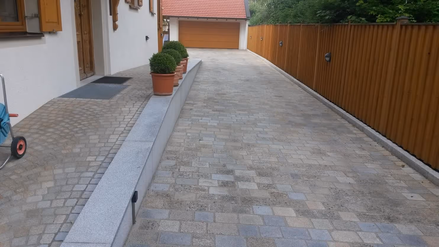 Příjezdová cesta s formátovanou žulovou dlažbou, obloženou zídkou a elegantním vstupem do domu s obloukovou dlažbou.