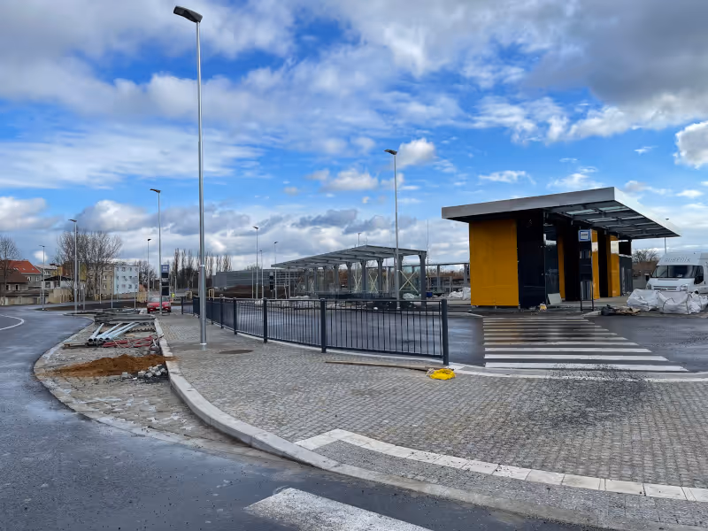 Autobusový terminál v Kralupech nad Vltavou během výstavby, s moderními přístřešky, žulovou dlažbou a veřejným osvětlením.