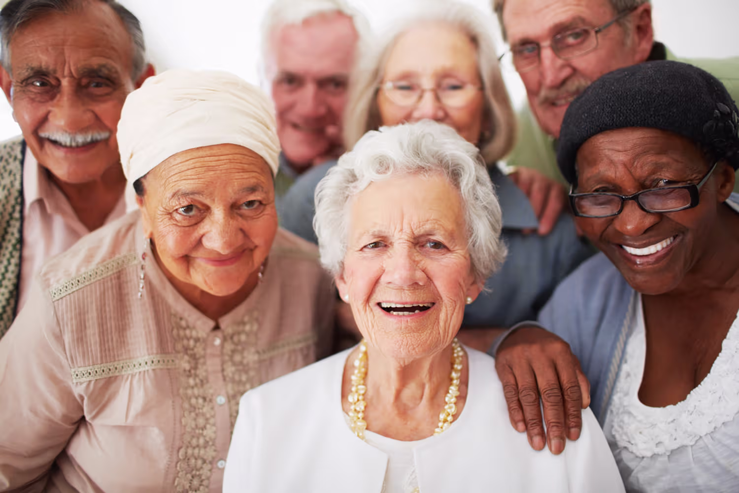 Group of six diverse elderly people smiling and posing closely together.