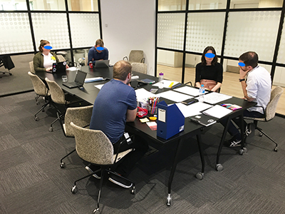 A photo of two people developing a simple scenario artefact on paper while other people observe and take notes.