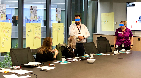 A photo of a group of people discussing and developing artefacts placed on a window and a wall.