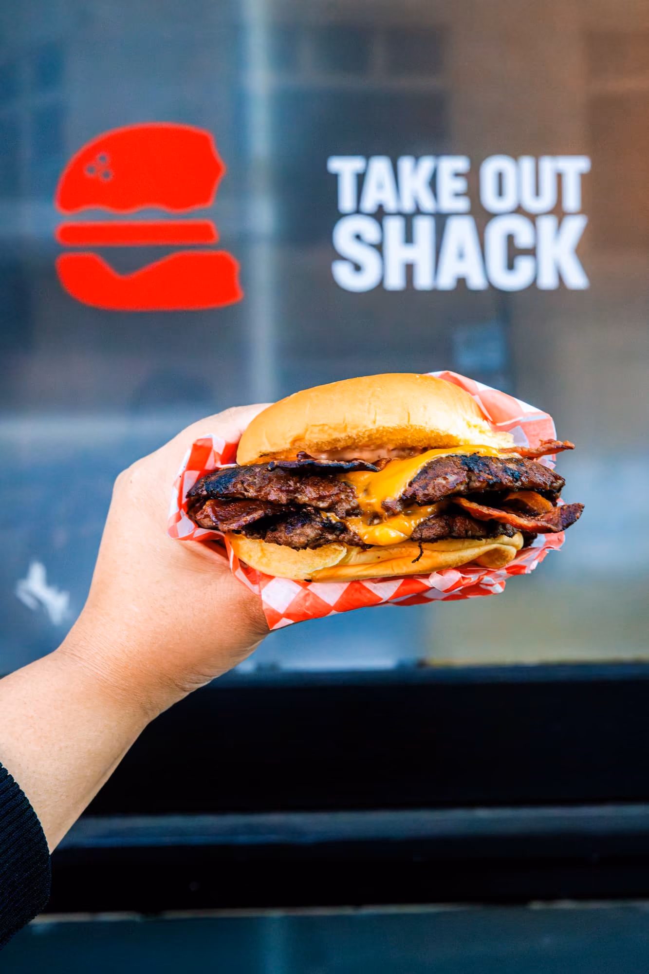 Person holding a smash burger in front of Take Out Shack in Vancouver, BC