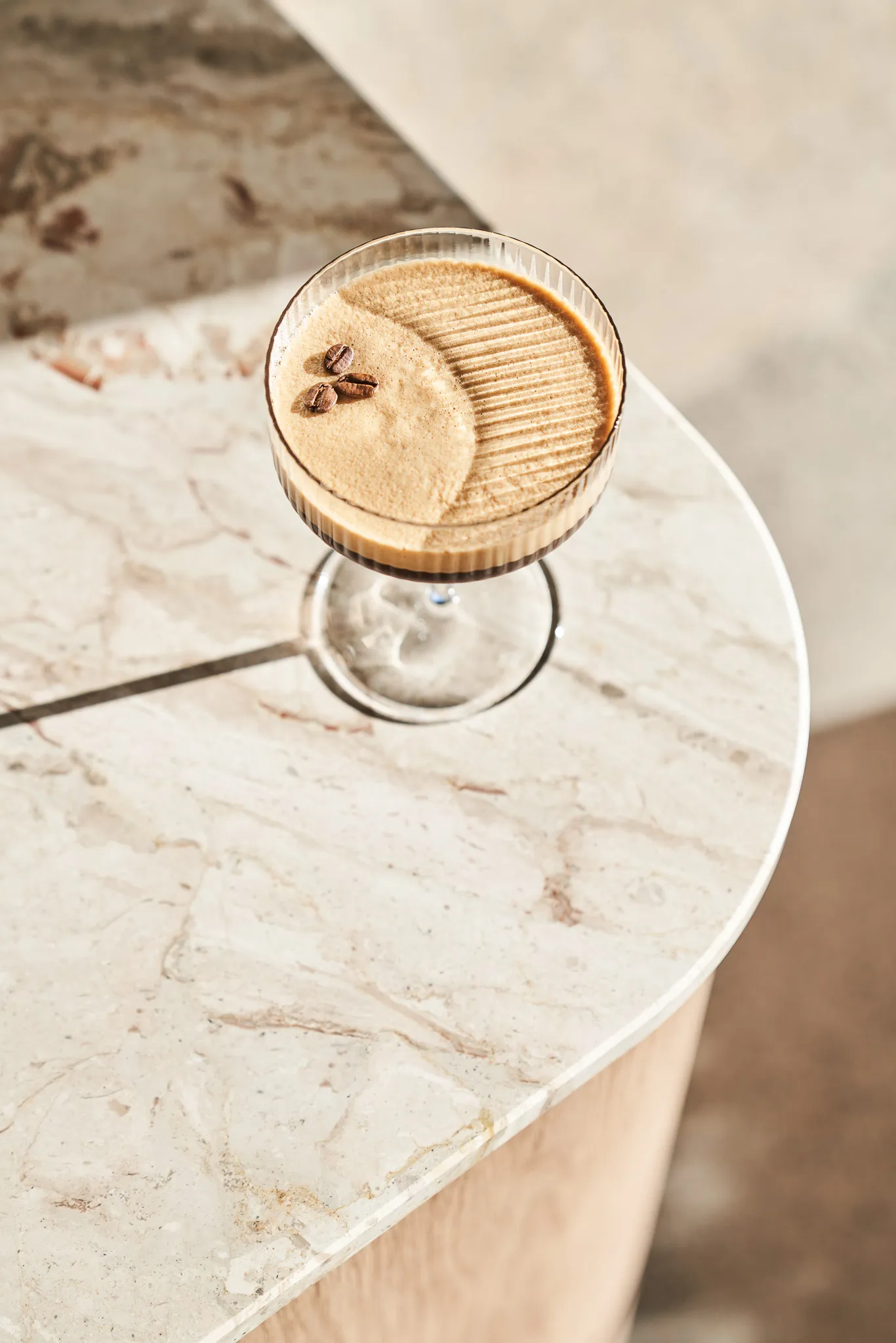 Cocktail glass with frothy coffee drink topped with three coffee beans on a marble countertop.