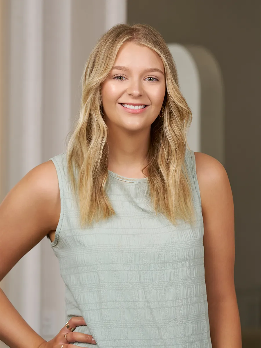 Smiling young woman with long blonde wavy hair wearing a sleeveless light green textured top.