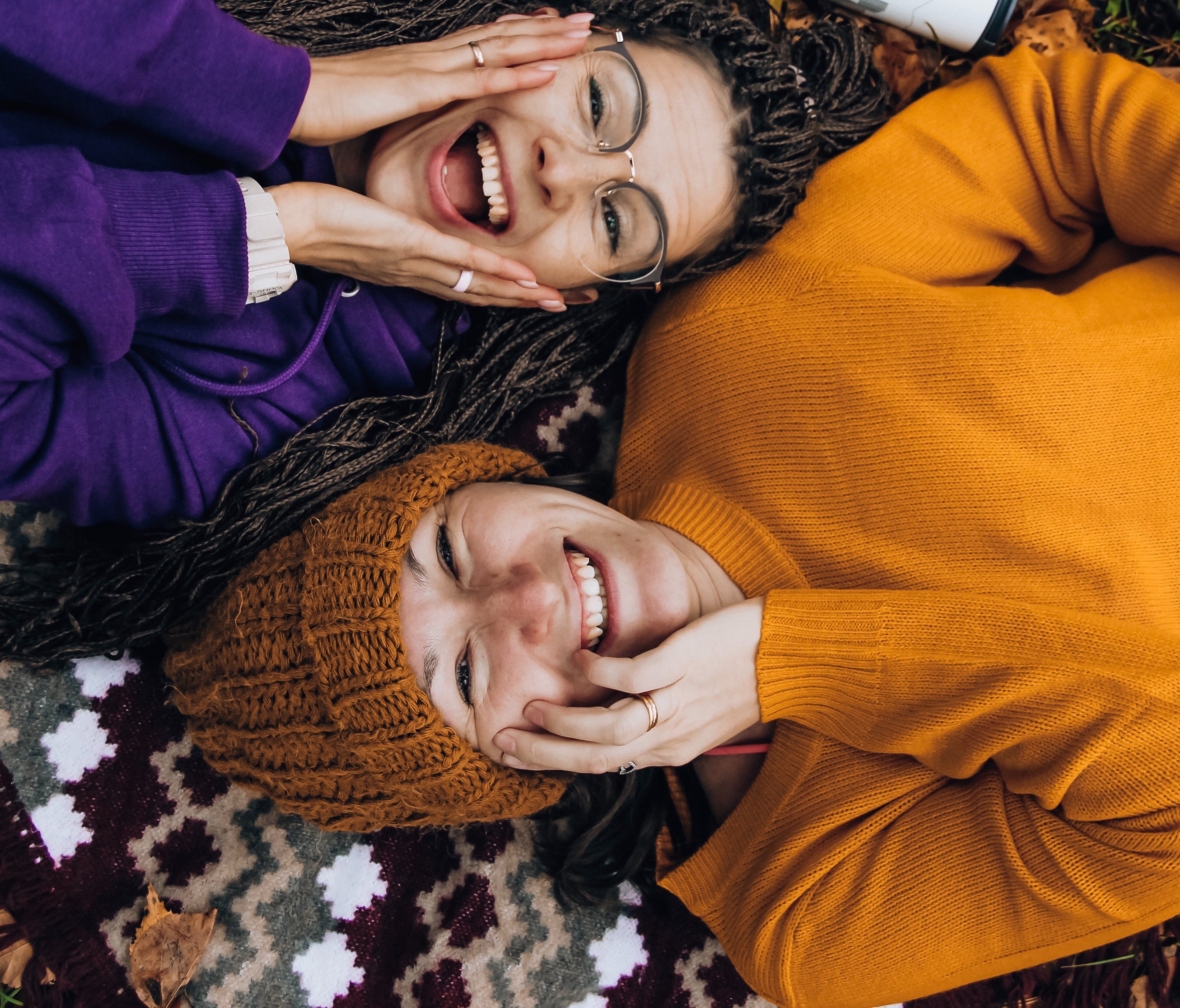Two women in yellow and purple sweaters, laying down opposite and smiling