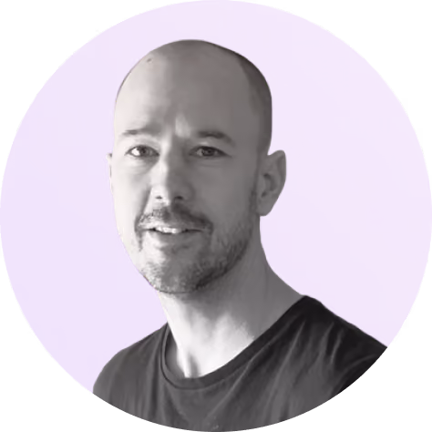 Portrait of a smiling bald man with a beard in front of a purple background.