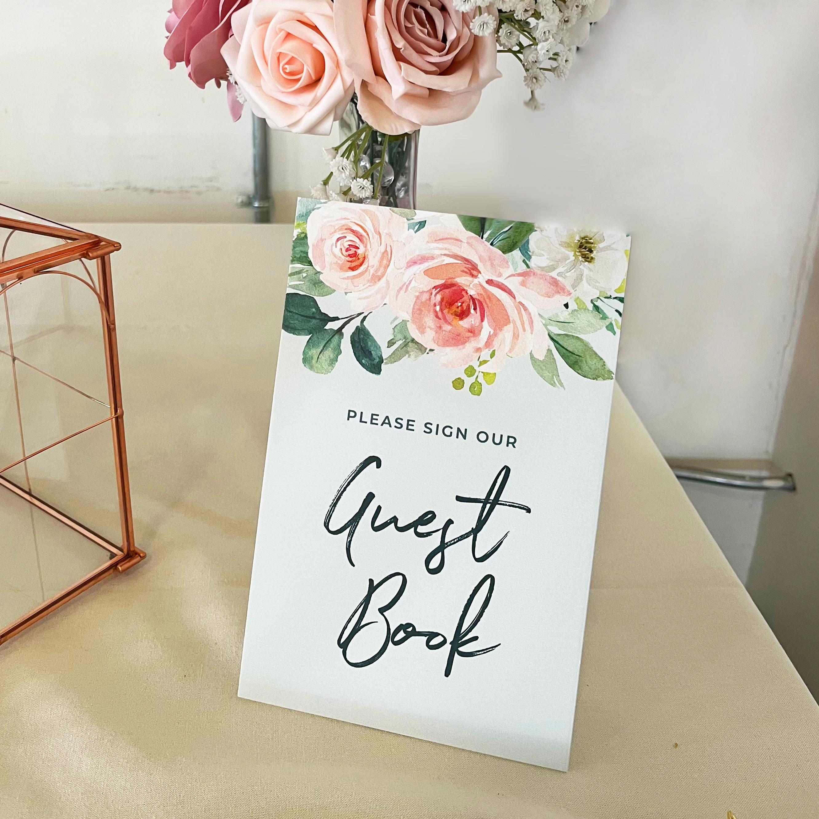 Photo of the guest book sign. Features watercolor flowers at the top and text that reads, "please sign our guest book"