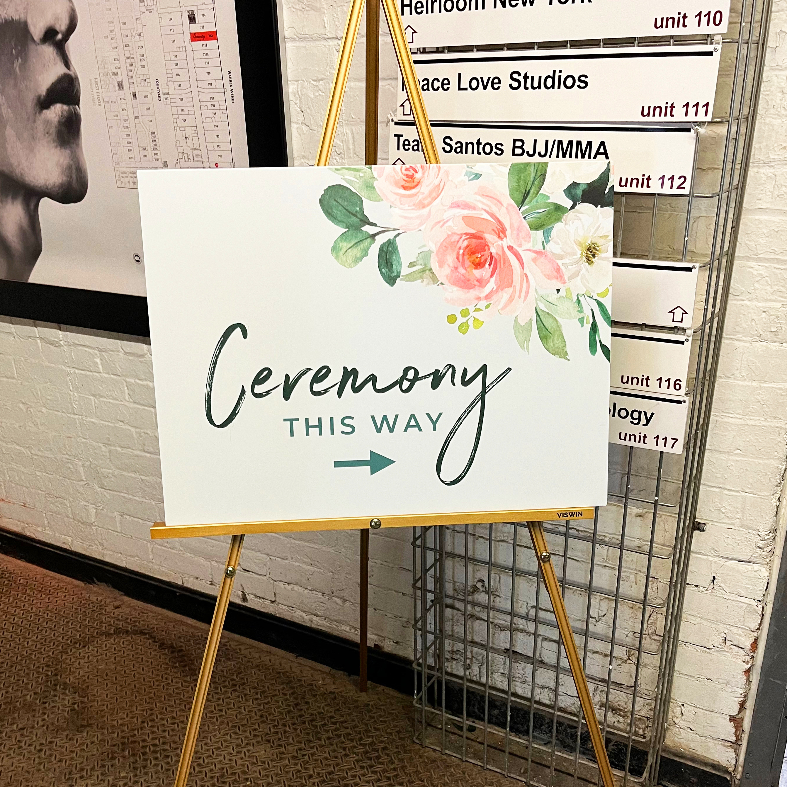 Photo of the ceremony sign. Features watercolor flowers a corner and text that reads, "ceremony this way"