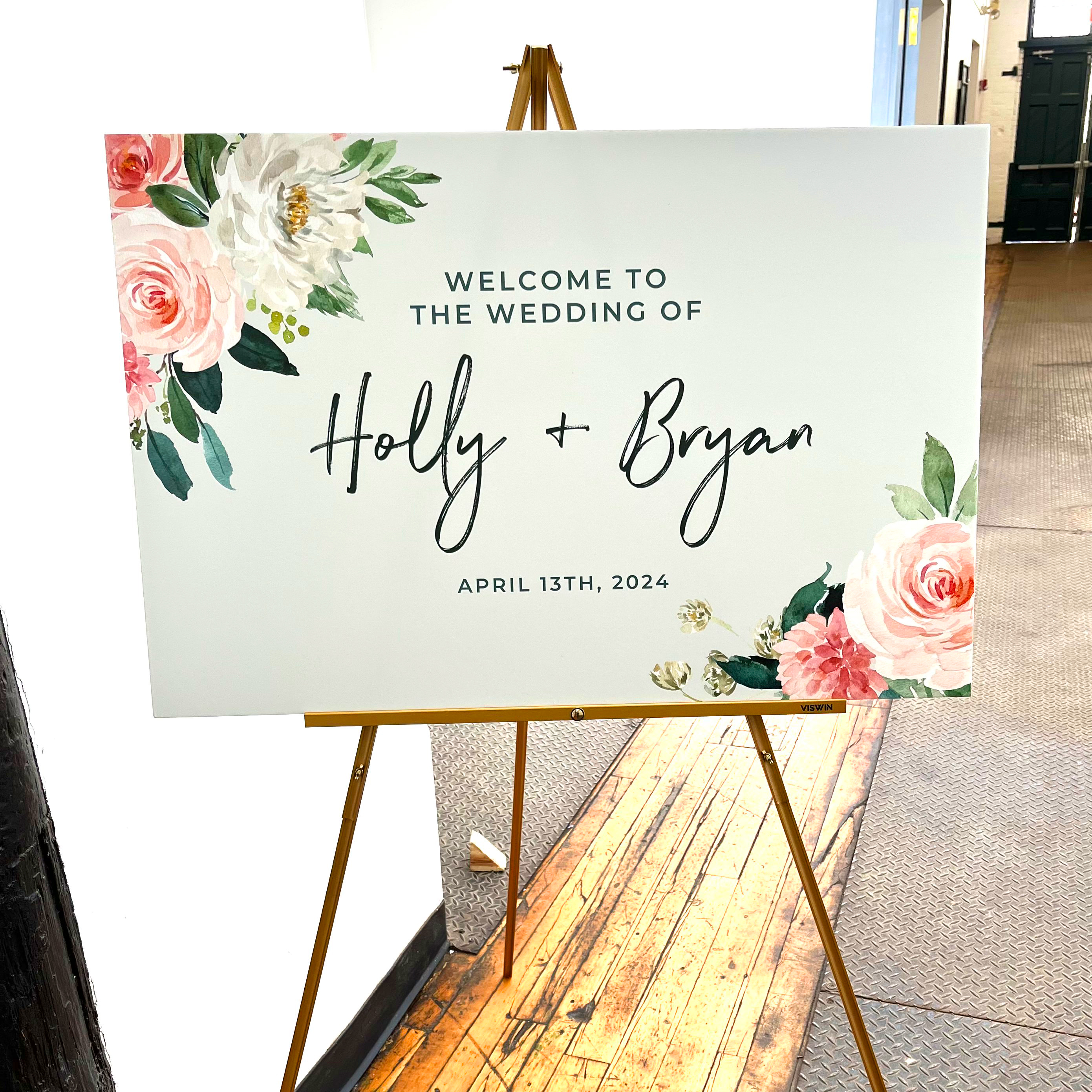 Photo of the main wedding welcome sign. Features watercolor flowers in corners and text that says "Welcome to the wedding of Holly and Bryan. April 13th, 2024"