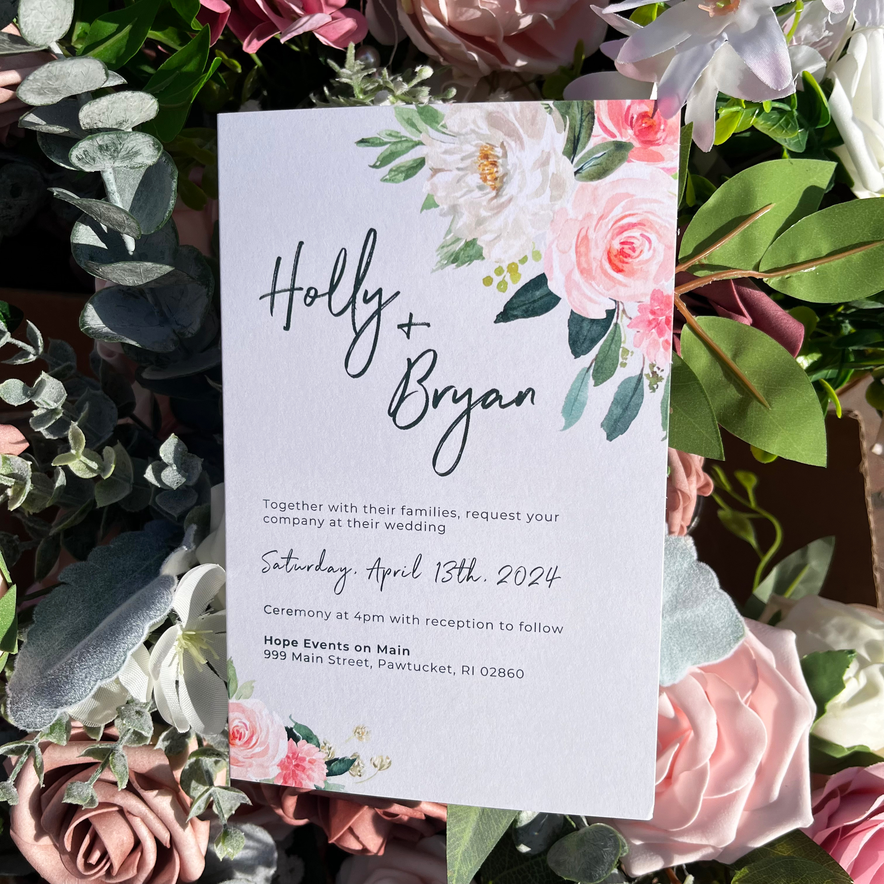 Photo of the front of the wedding invitation. Features watercolor flowers in the corners and text that reads, "Holly and Bryan, together with their families, request your company at their wedding," followed by date and location information
