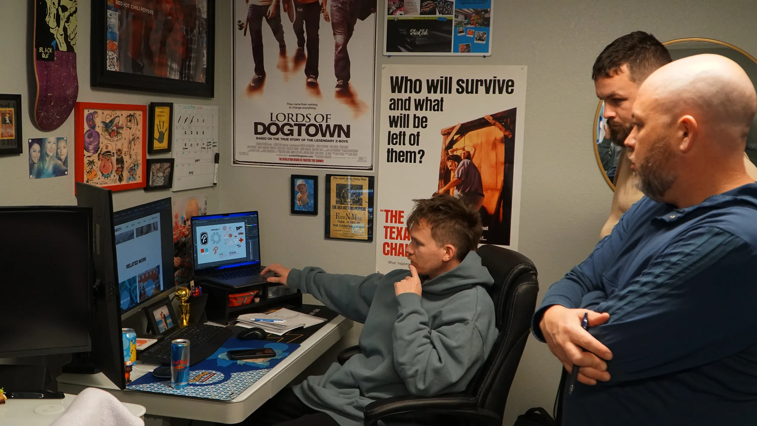 Three men focused on computer screens in a decorated office with posters and skateboards on the wall.
