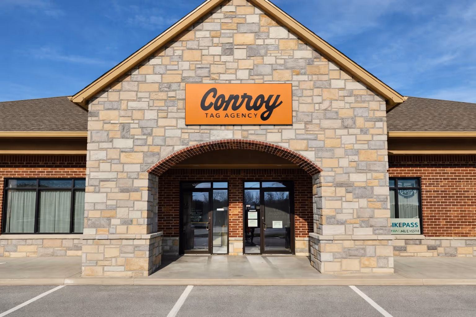Stone and brick building entrance with an orange sign reading 'Conroy Tag Agency' above double glass doors.
