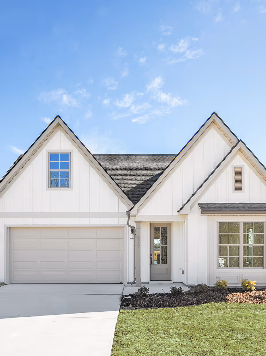 White modern house with a double garage, gray front door, large front window, and neatly trimmed lawn under a blue sky.