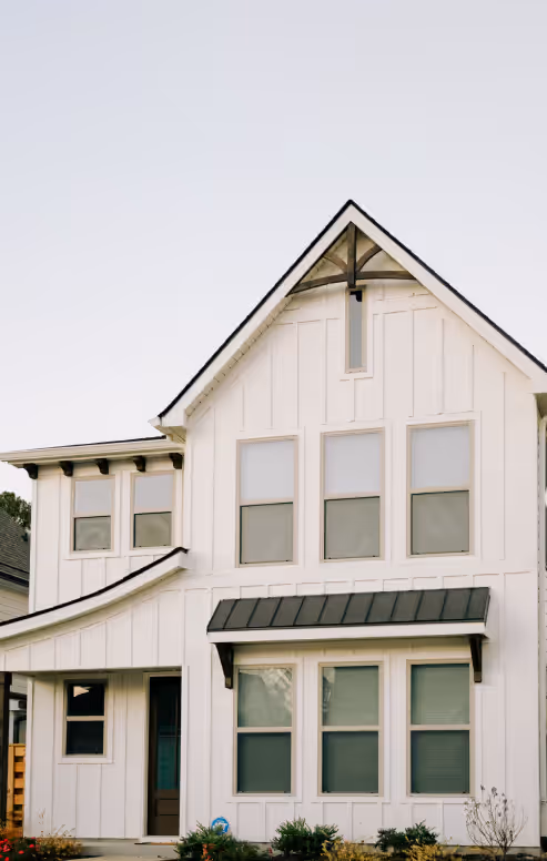 Modern white two-story house with multiple windows and a small black awning over the front window.
