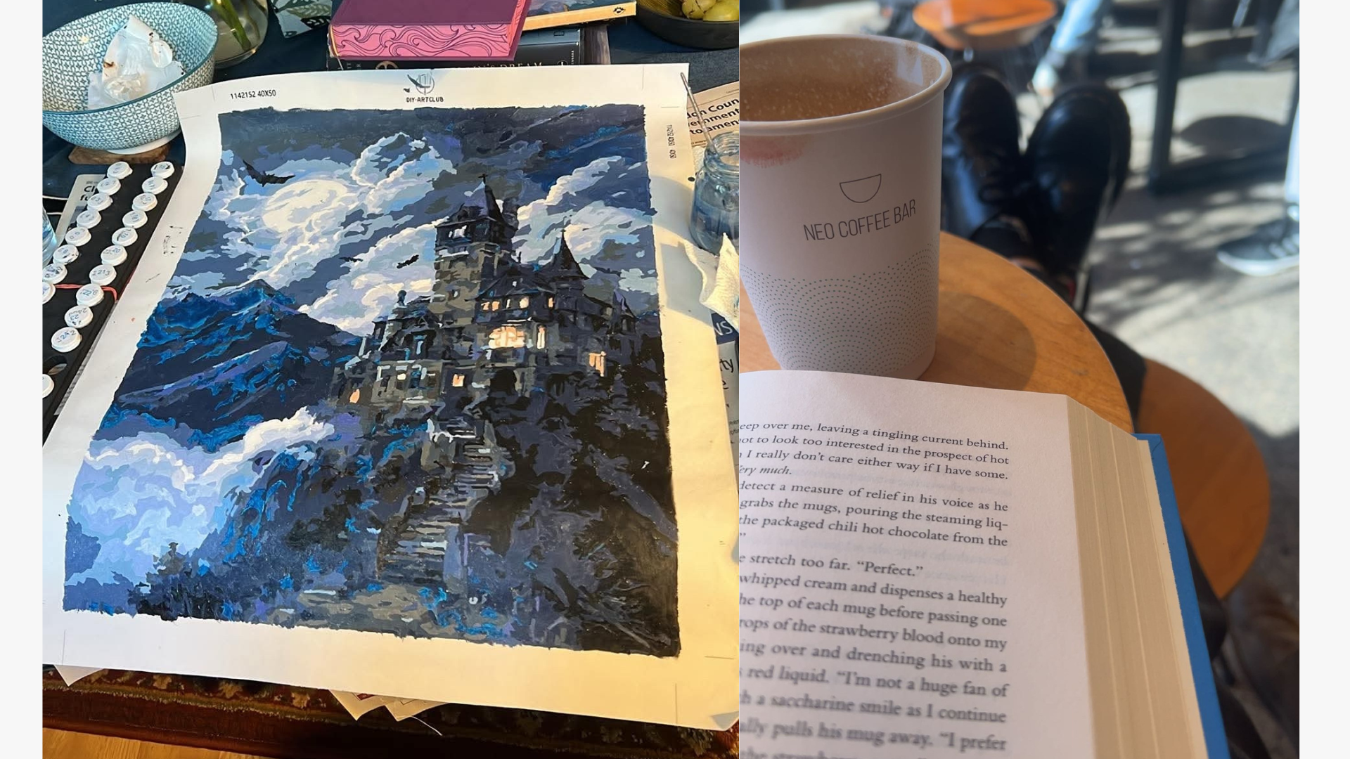 A paint-by-numbers project featuring a dark, moody castle scene at night sits on a table, surrounded by paint pots and brushes. Next to it, a café scene with a book, a cup of coffee, and someone's crossed legs is visible, suggesting a relaxed atmosphere.