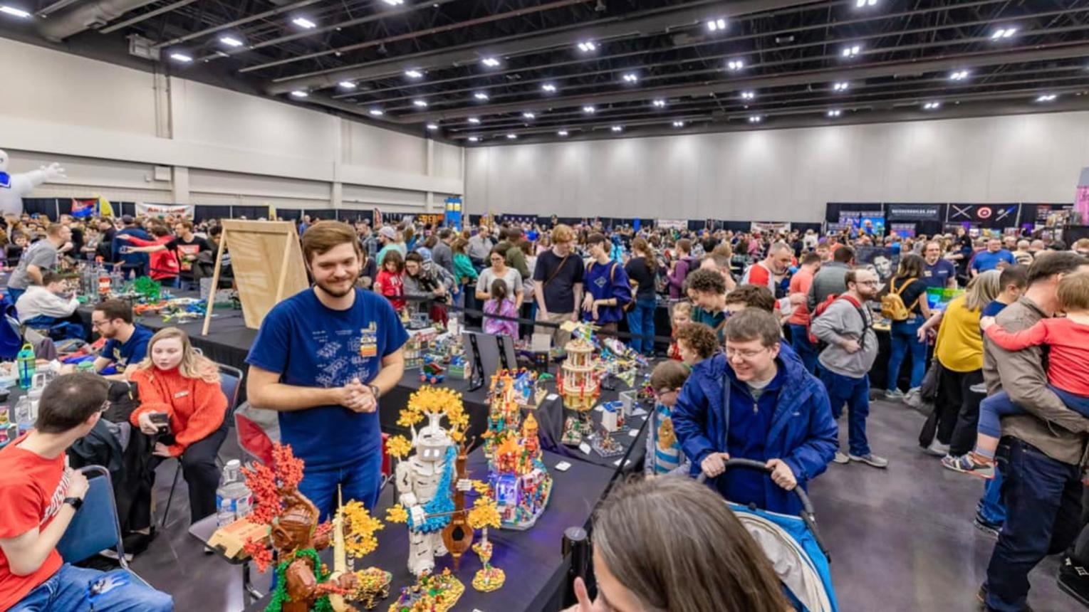 An event in a large indoor venue where attendees explore booths and displays. People are interacting with exhibits, surrounded by vibrant decorations and bustling activity.