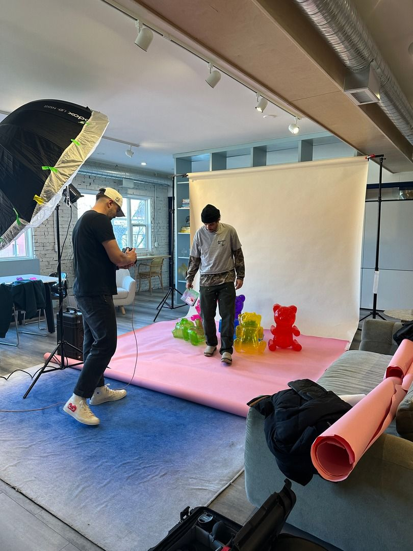 A photographer prepares to take photos in a studio featuring colourful gummy bear sculptures arranged on a pink backdrop. The room is equipped with professional lighting and photo equipment.