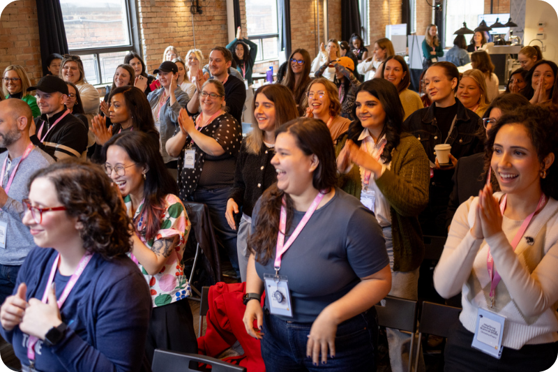 A large crowd in a conference setting claps.