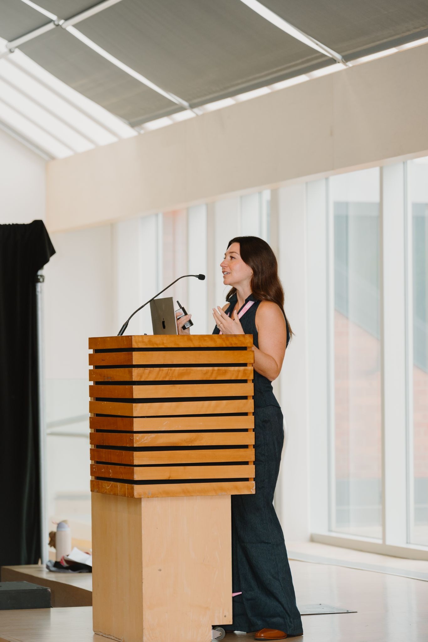 Woman giving a presentation at a podium in a modern conference room with large windows.