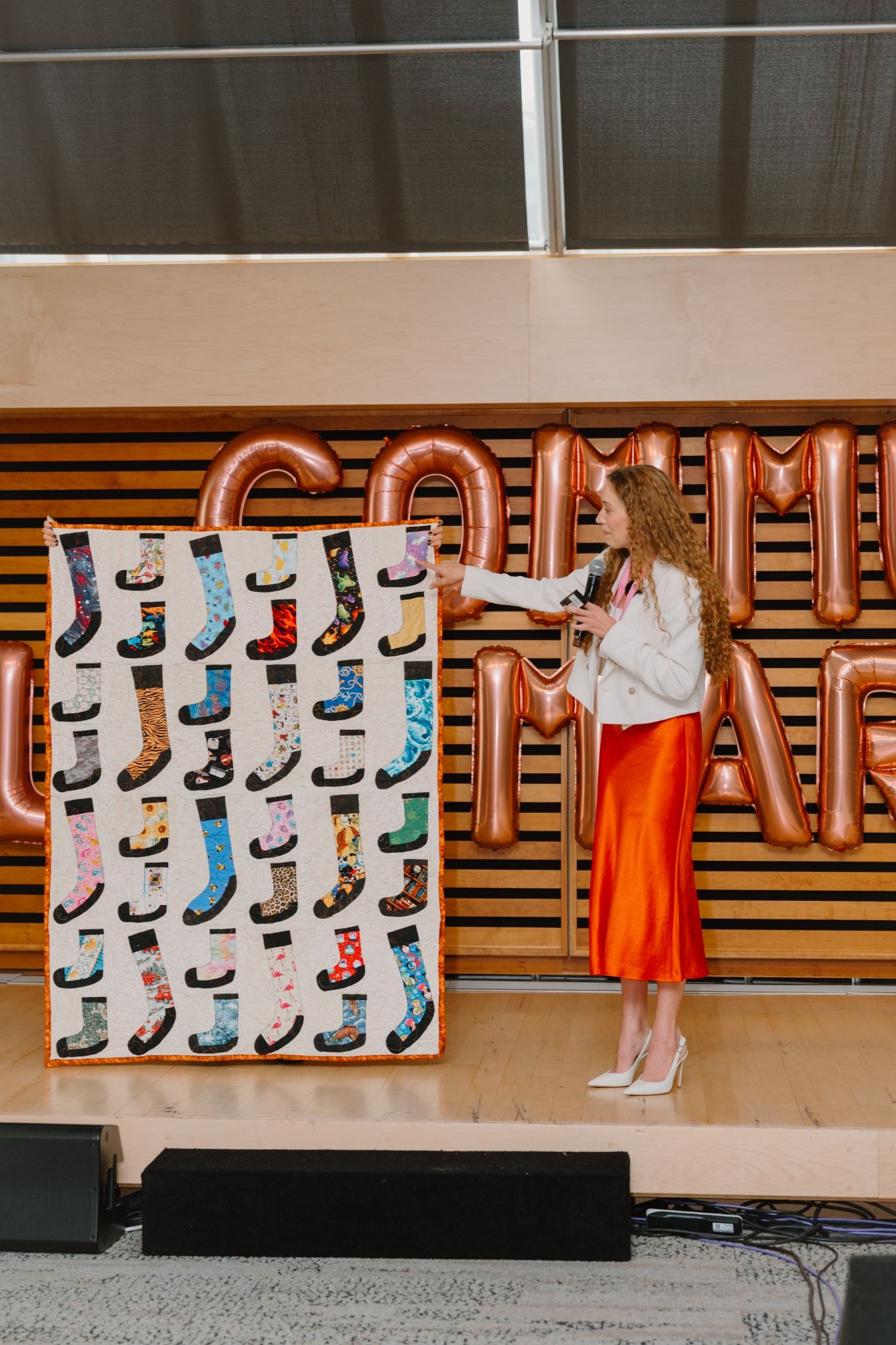 A speaker gestures toward a board displaying various patterned socks, set against a modern interior backdrop.