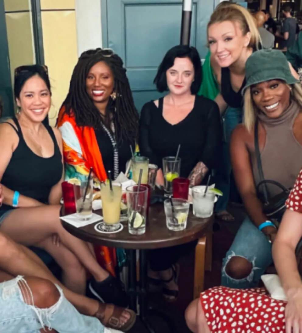 Social media agency director Daria and her team members enjoying a celebratory drink around a small wooden table after a day at the office.