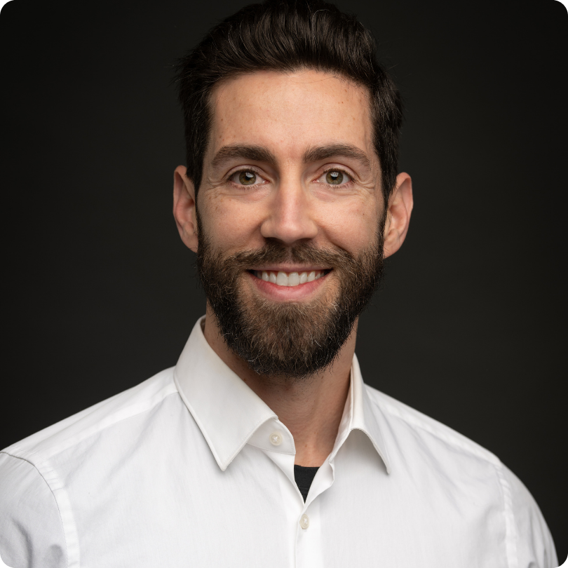 Jonas Eyford standing in front of a black background, smiling at the camera in a white button up shirt