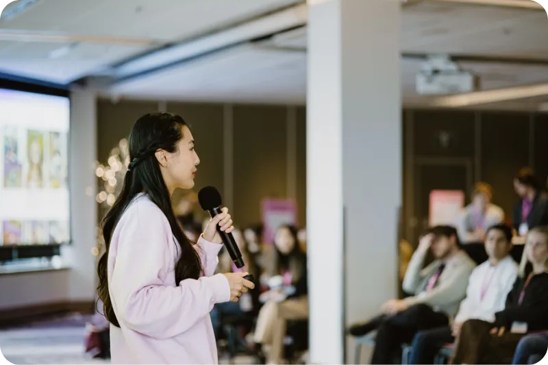 Jessica stands in front of a crowd holding a microphone.