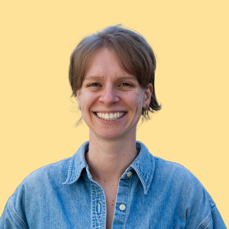 Annie Warner smiles in her headshot. The photo is emphasized by a bright pink drop-shadow.