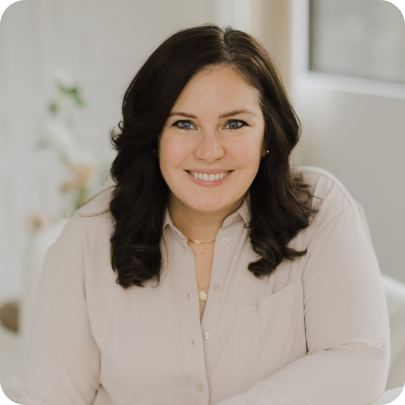 A woman with dark hair smiles for the camera. She wears a cream button up top.