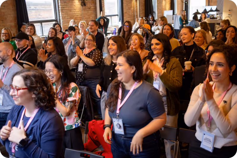 A large crowd of people smile and clap at a conference.