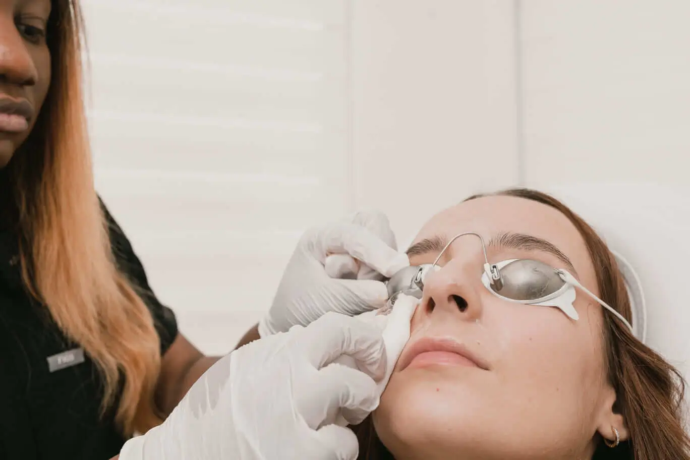 A woman getting her IPL done by a woman in a black shirt.