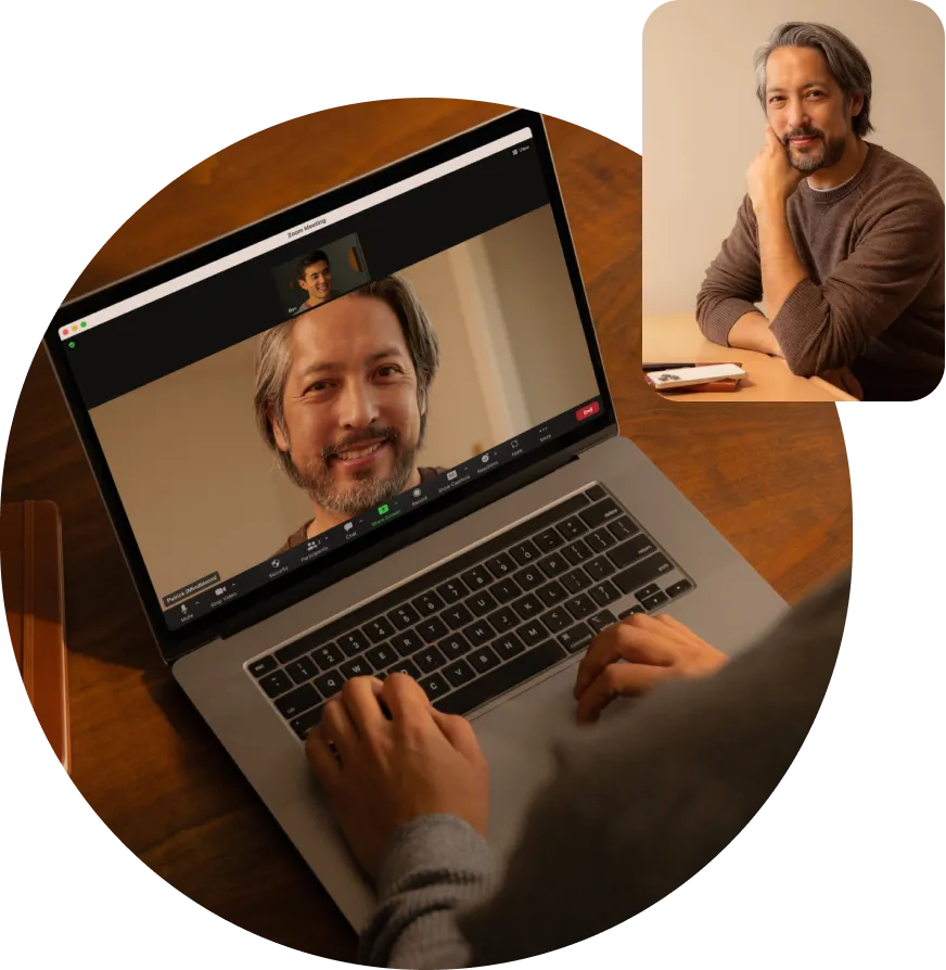 Person attending a Zoom video call on a laptop, showing a smiling man with gray hair and a beard, with an inset image of the same man seated at a table.