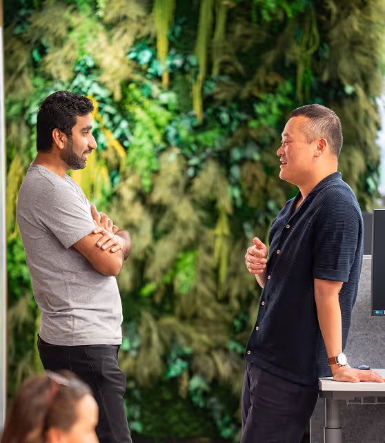 Two Q-CTRL colleagues engaged in conversation in an office with a green plant wall background.