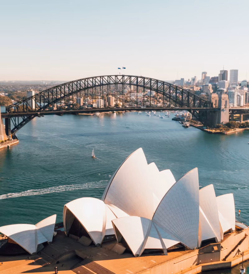 Sydney Opera House with sail-like roof structures and Sydney Harbour Bridge in the background over water.