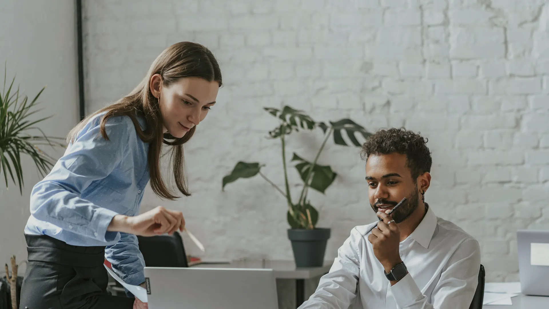Woman in blue shirt and man in white shirt working together on a laptop in an office.