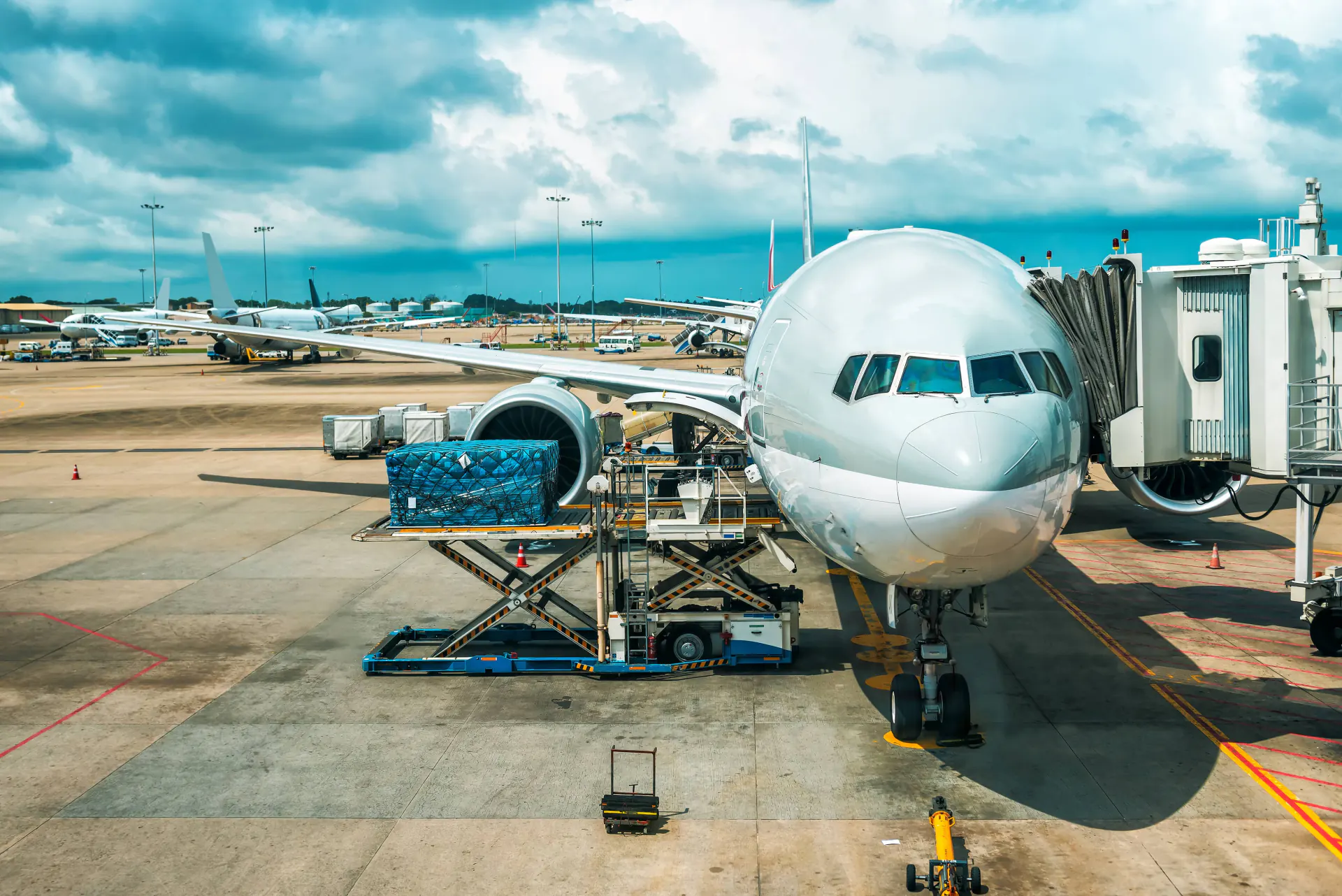 Front view of a large airplane at gate with jet bridge and cargo loading ramp on airport tarmac.