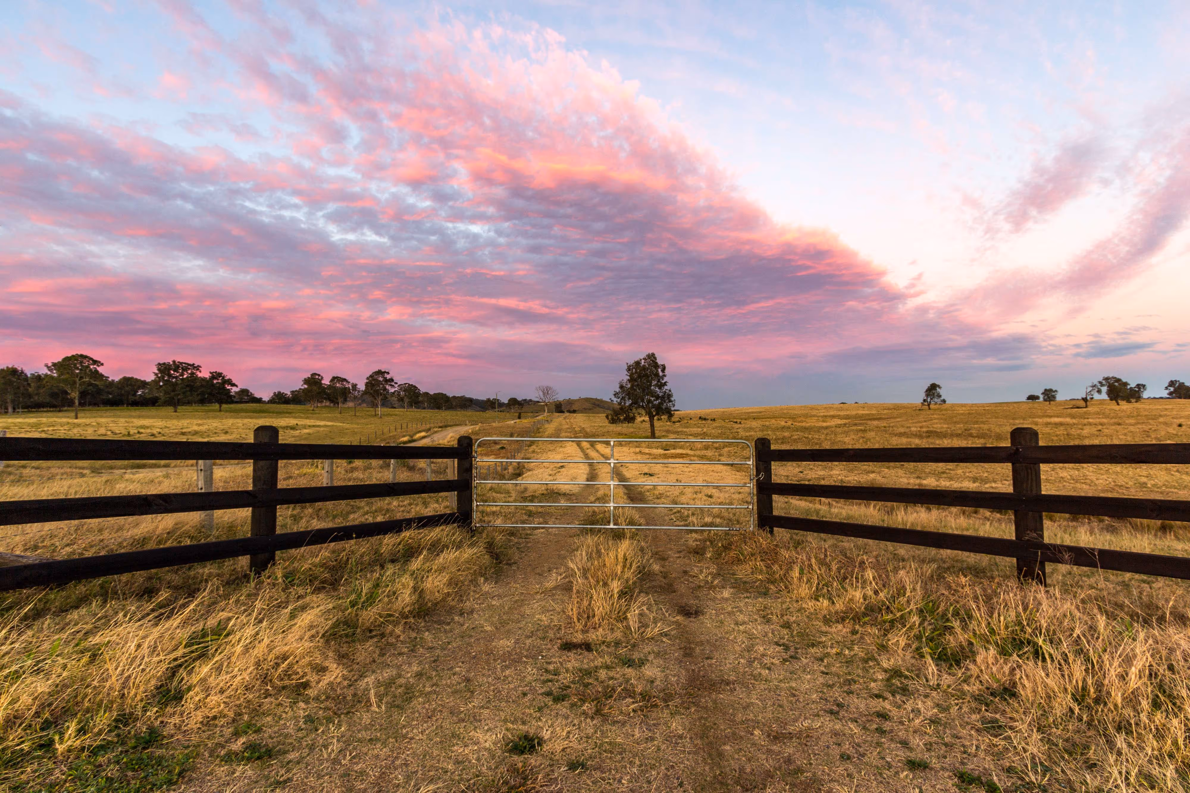 Scenic image of a stunning sunset with a gate leading to a farm. The picture captures the beauty of the countryside, with warm sunset colors painting the sky and a peaceful farm setting.