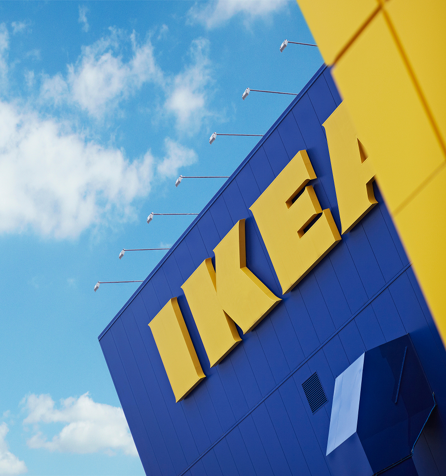 Close-up angled view of a building exterior with large yellow IKEA letters on a blue wall under a partly cloudy sky.
