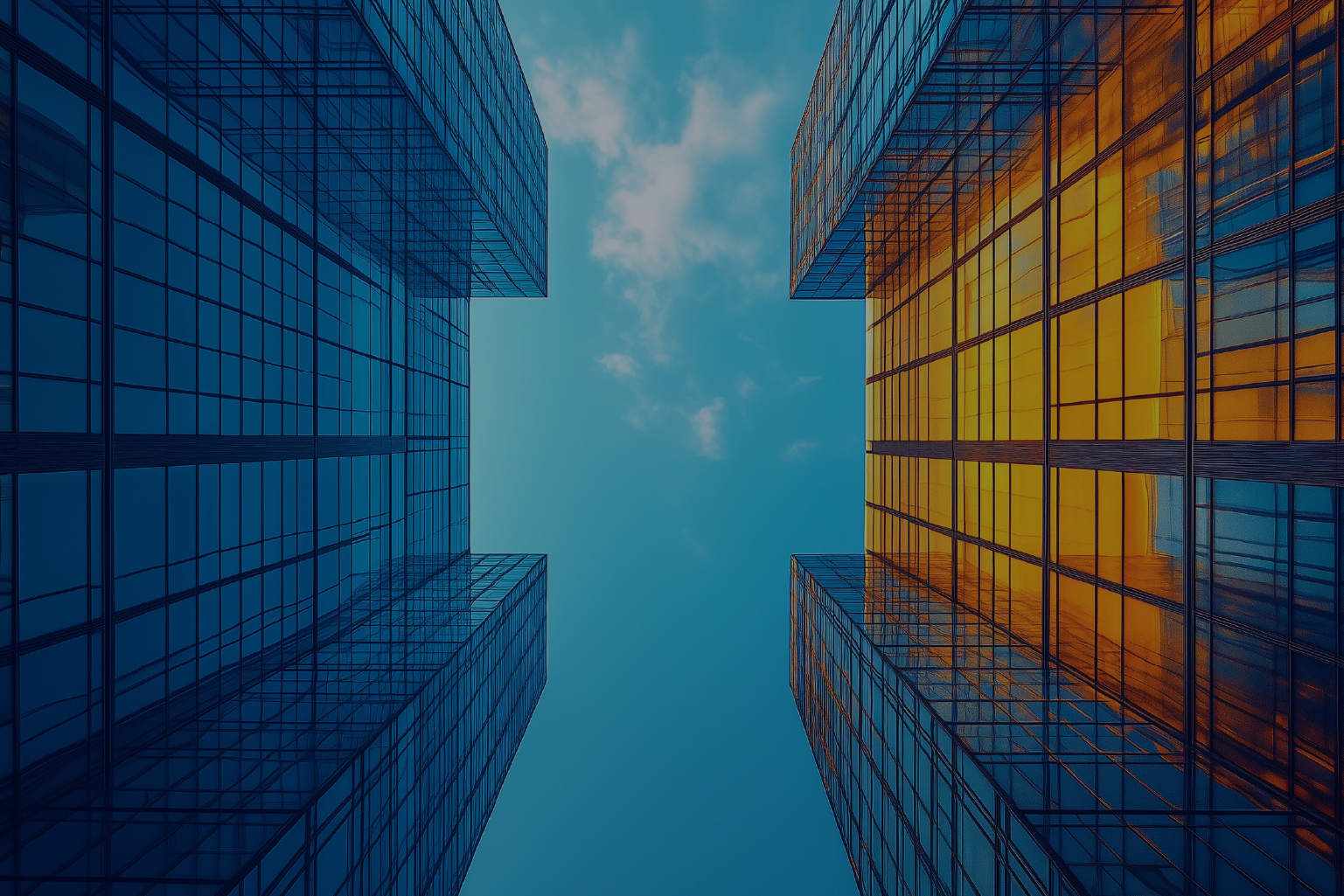 View looking up between two modern skyscrapers with blue and orange reflective glass windows against a bright blue sky with some clouds.
