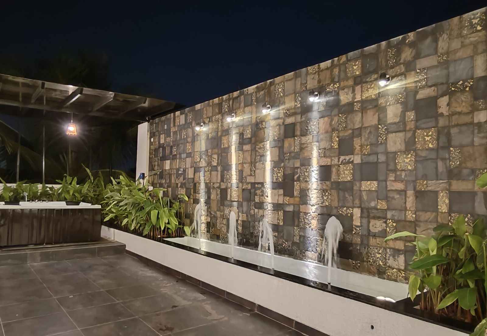 Private rooftop deck at night with a lit stone water wall and plants, penthouse party venue in Bangalore