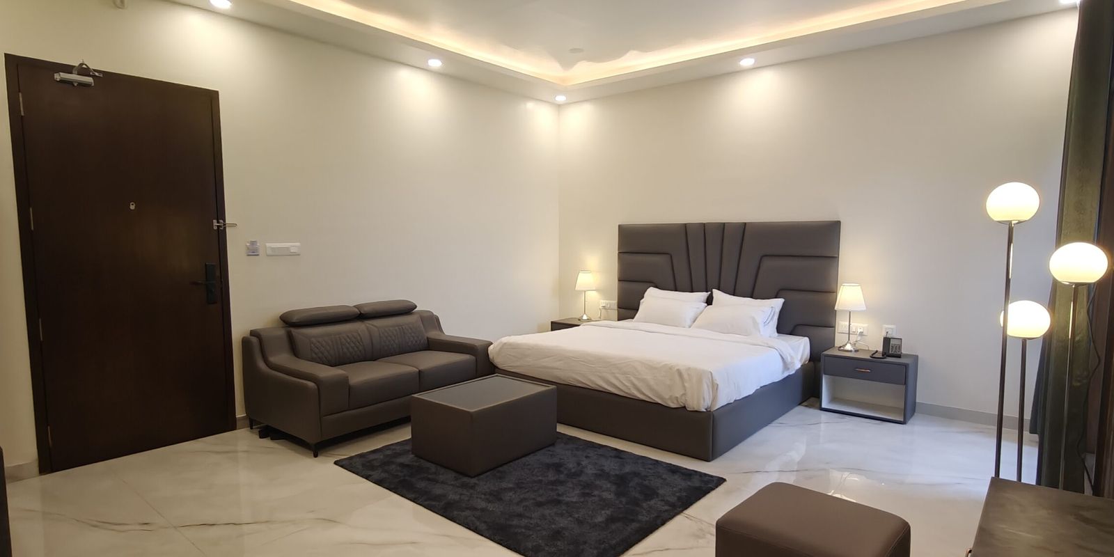 Bright hotel room with a two-seater sofa, bed and floor lamps on Thanisandra Main Road