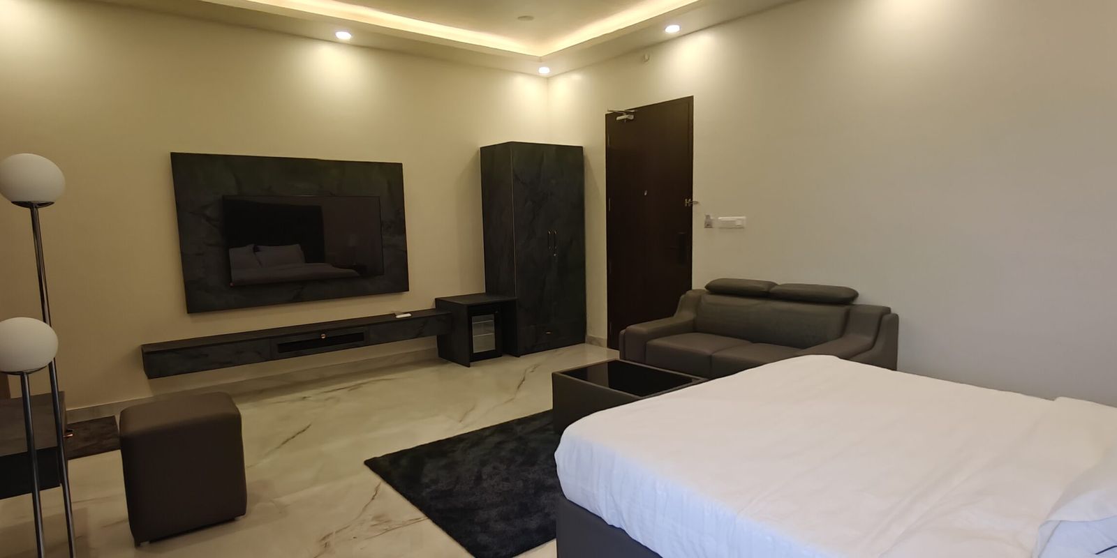 Hotel room with a TV wall, wardrobe and sofa seating in North Bangalore
