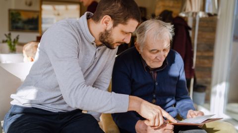 Un homme plus jeune accompagne une personne âgée en lui expliquant un document posé sur la table.