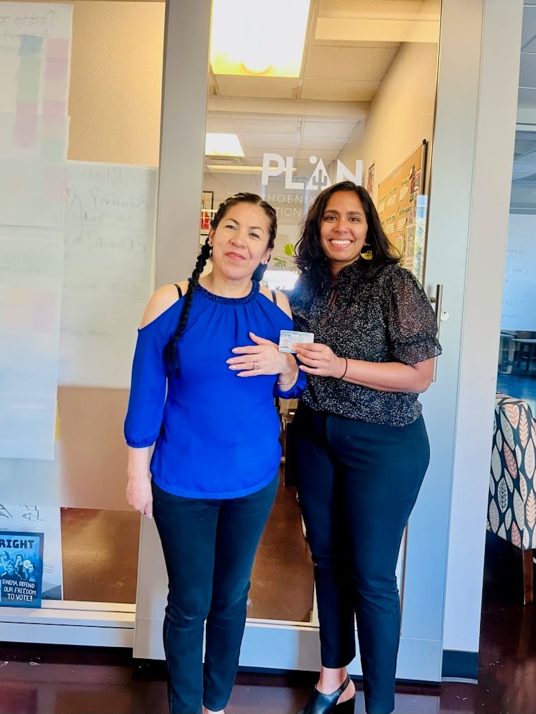 Sonia and her lawyer holding up her green card, smiling.