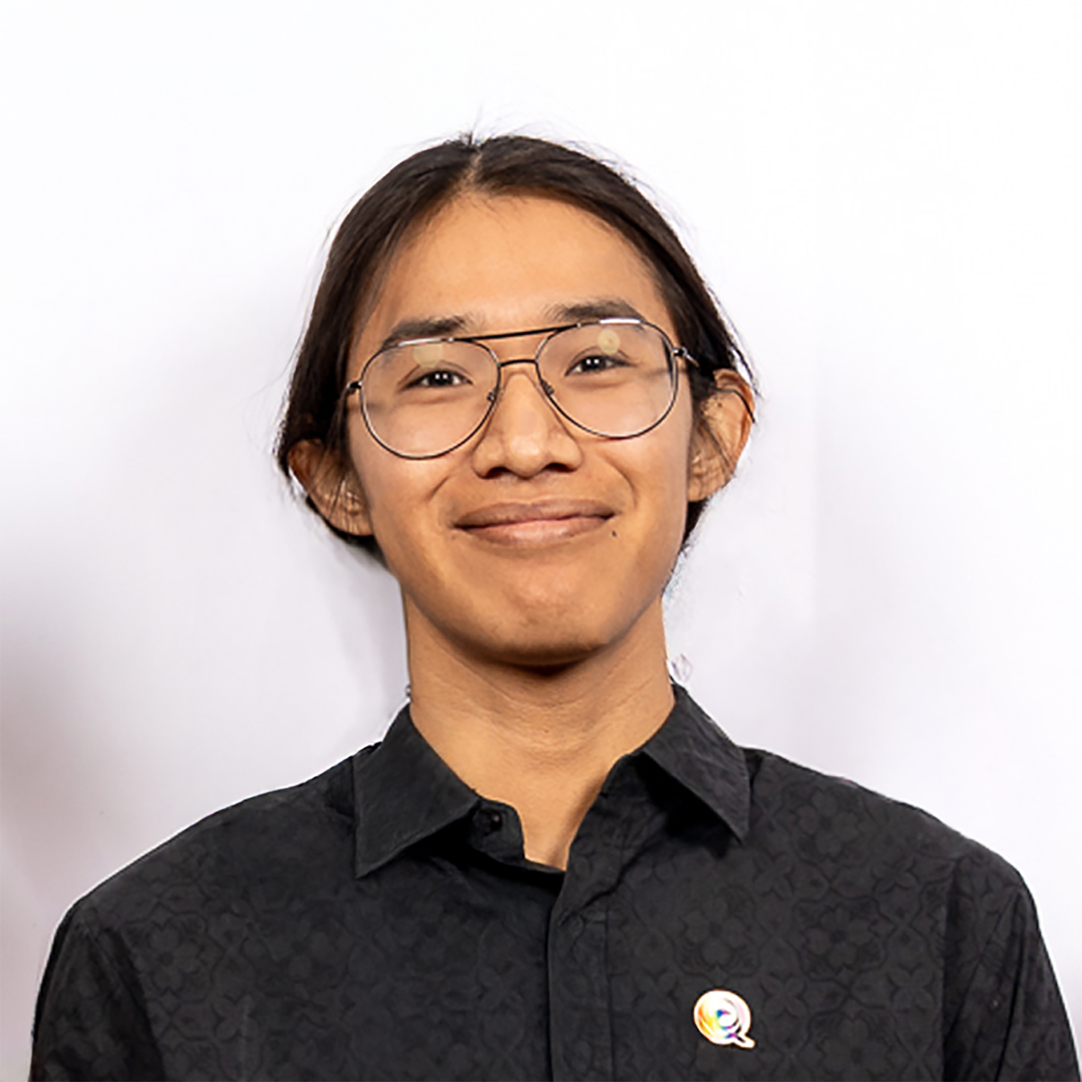 Primer plano de un hombre sonriendo sobre fondo blanco. Lleva camisa negra y gafas.