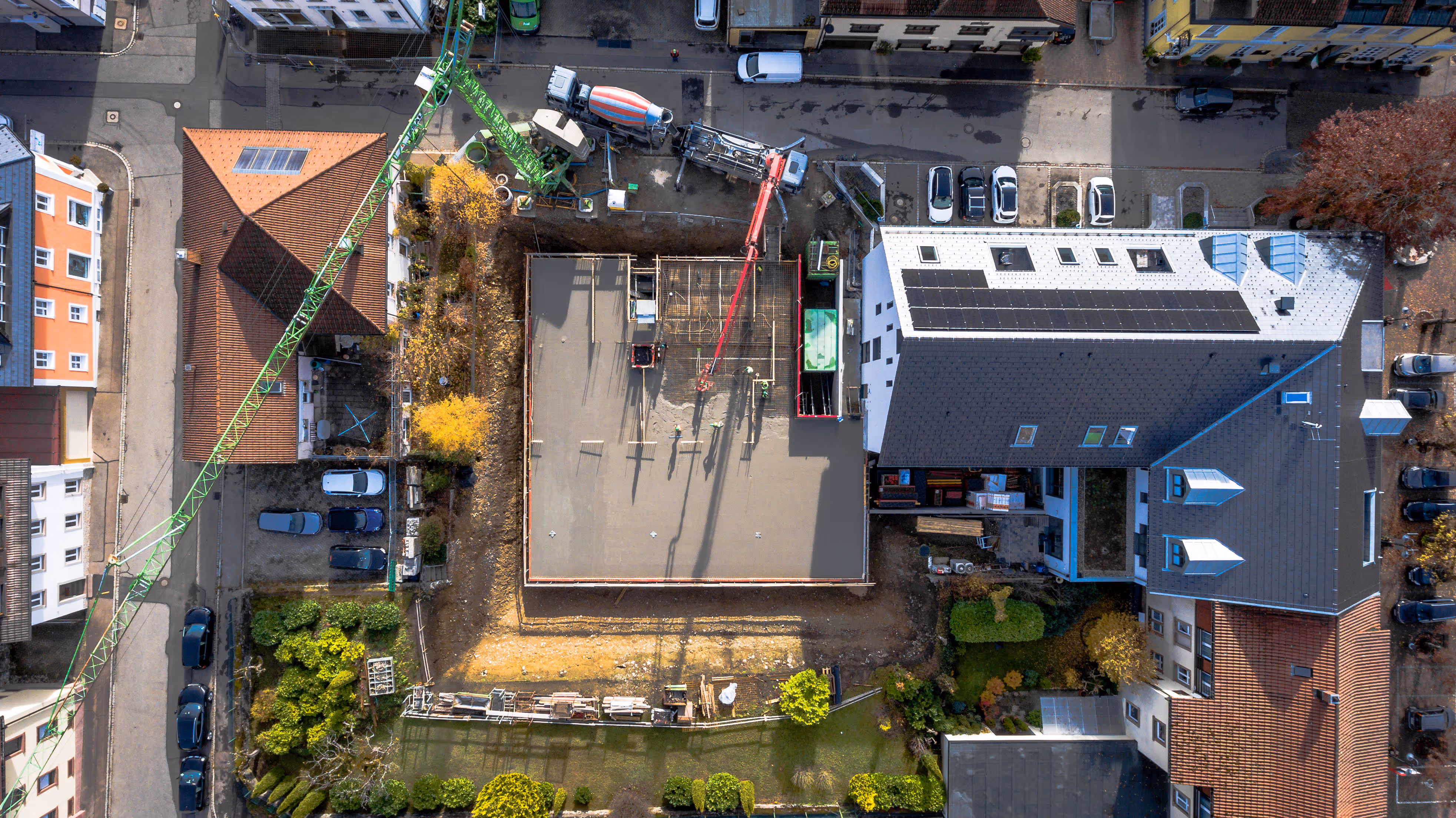 Baustelle aus der Vogelperspektive, Betonboden wird gegossen, mehrere Bauarbeiter, ein Betonmischer und ein Pumpwagen im Einsatz.