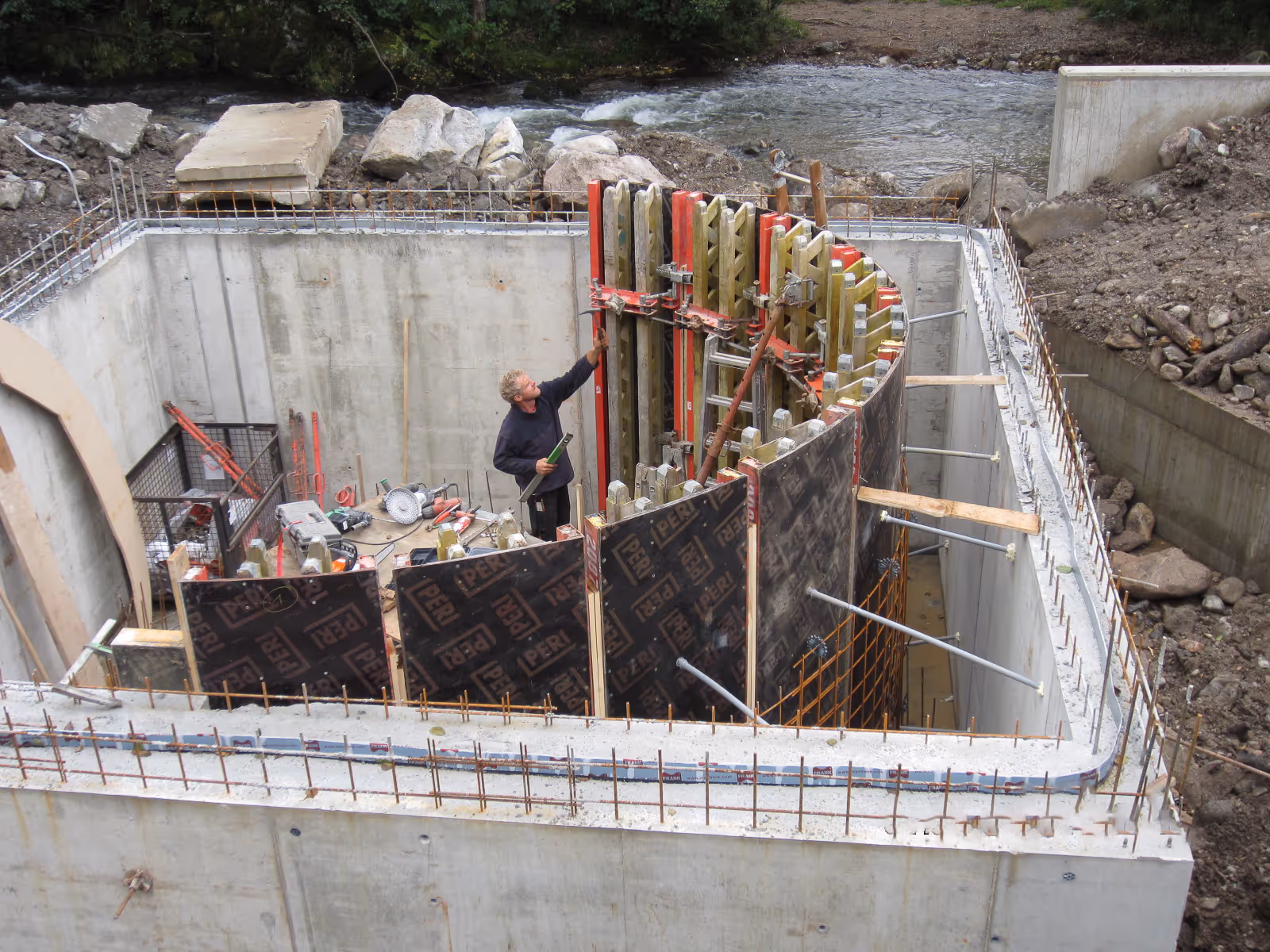 Arbeiter richtet Schalung an gebogener Betonwand aus.
