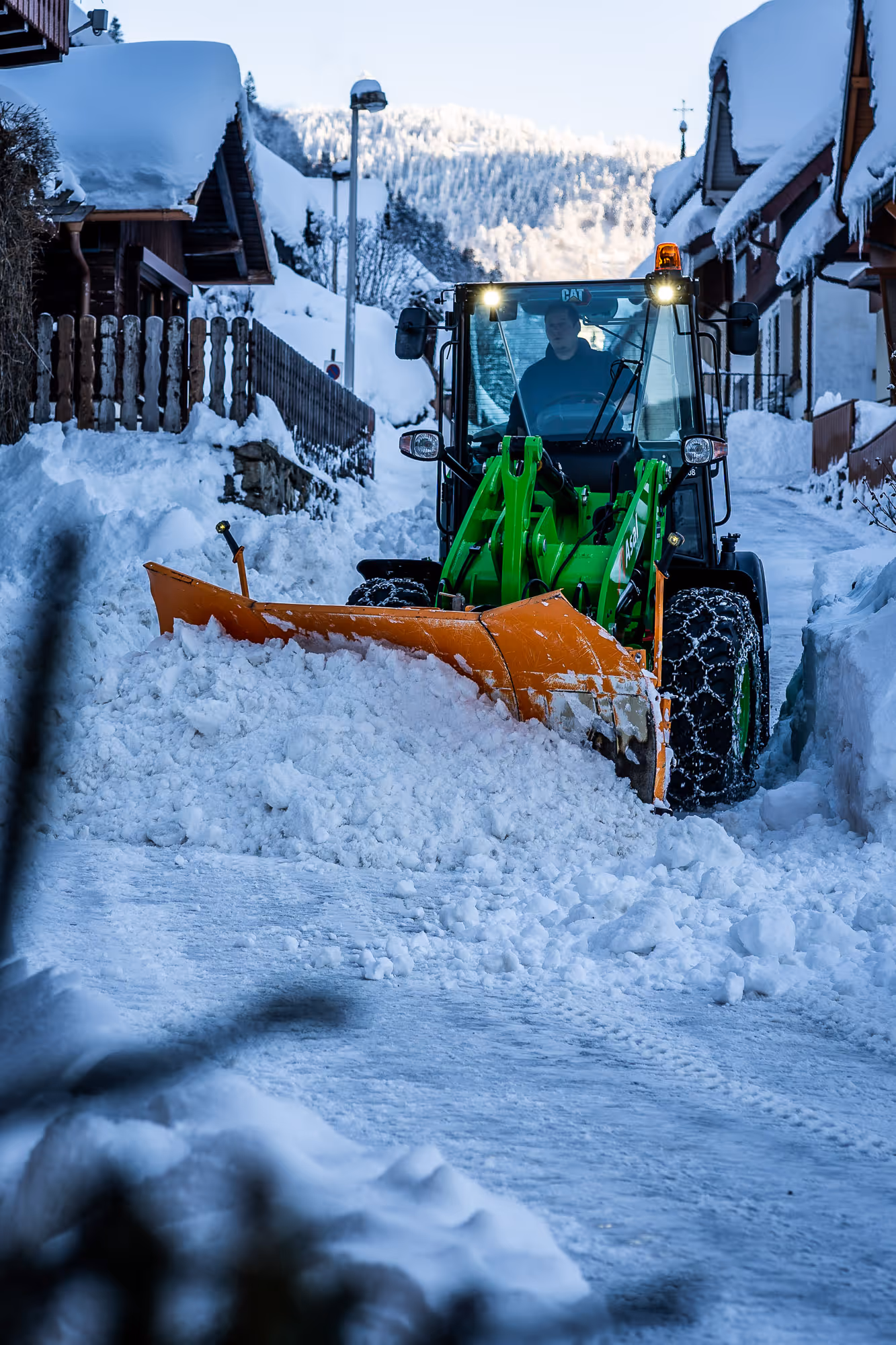 Radlader mit Schneeschild räumt Schnee vor Häusern im Winter.