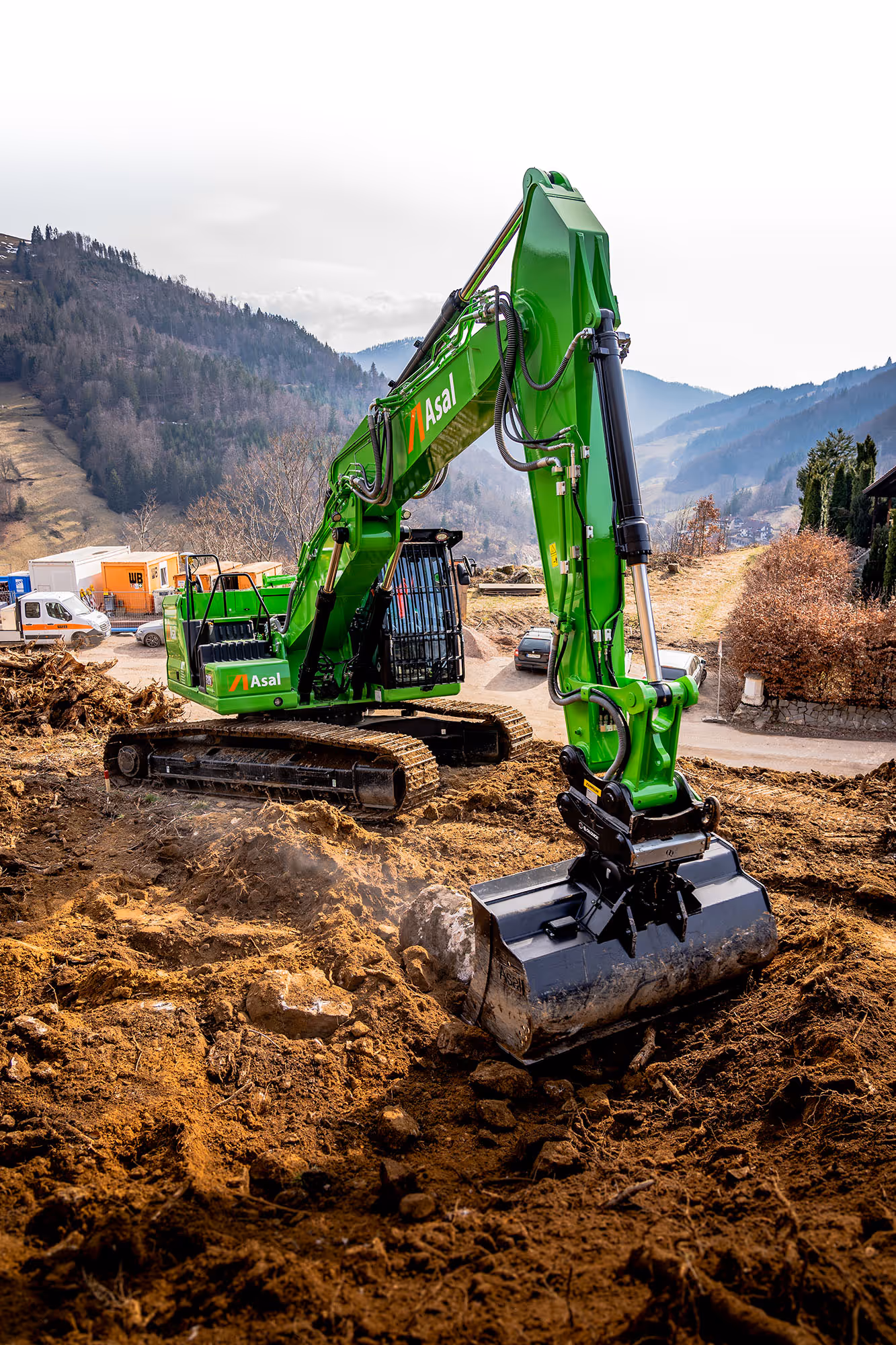 Grüner Asal-Bagger beim Tiefbau-Einsatz in hügeliger Landschaft.